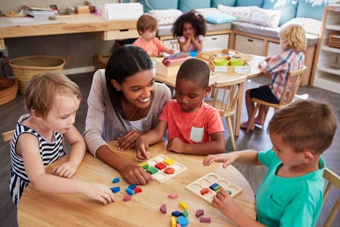 Teacher helping young children sort colorful shapes during a classroom activity.