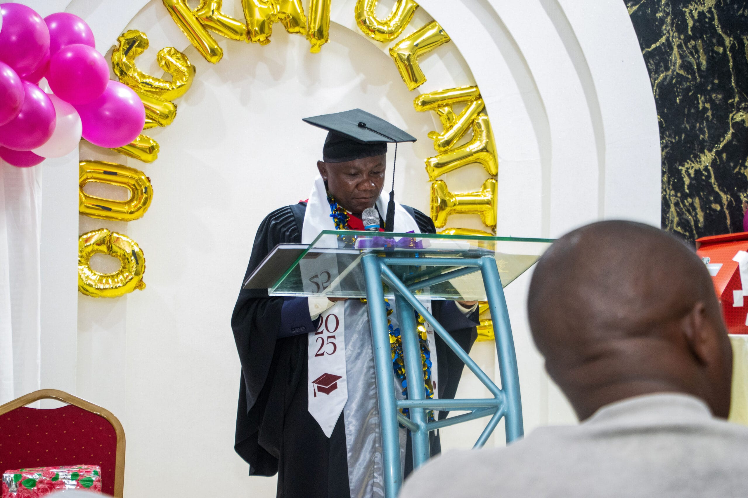Graduate delivering a speech at a podium during a decorated 2025 graduation ceremony.