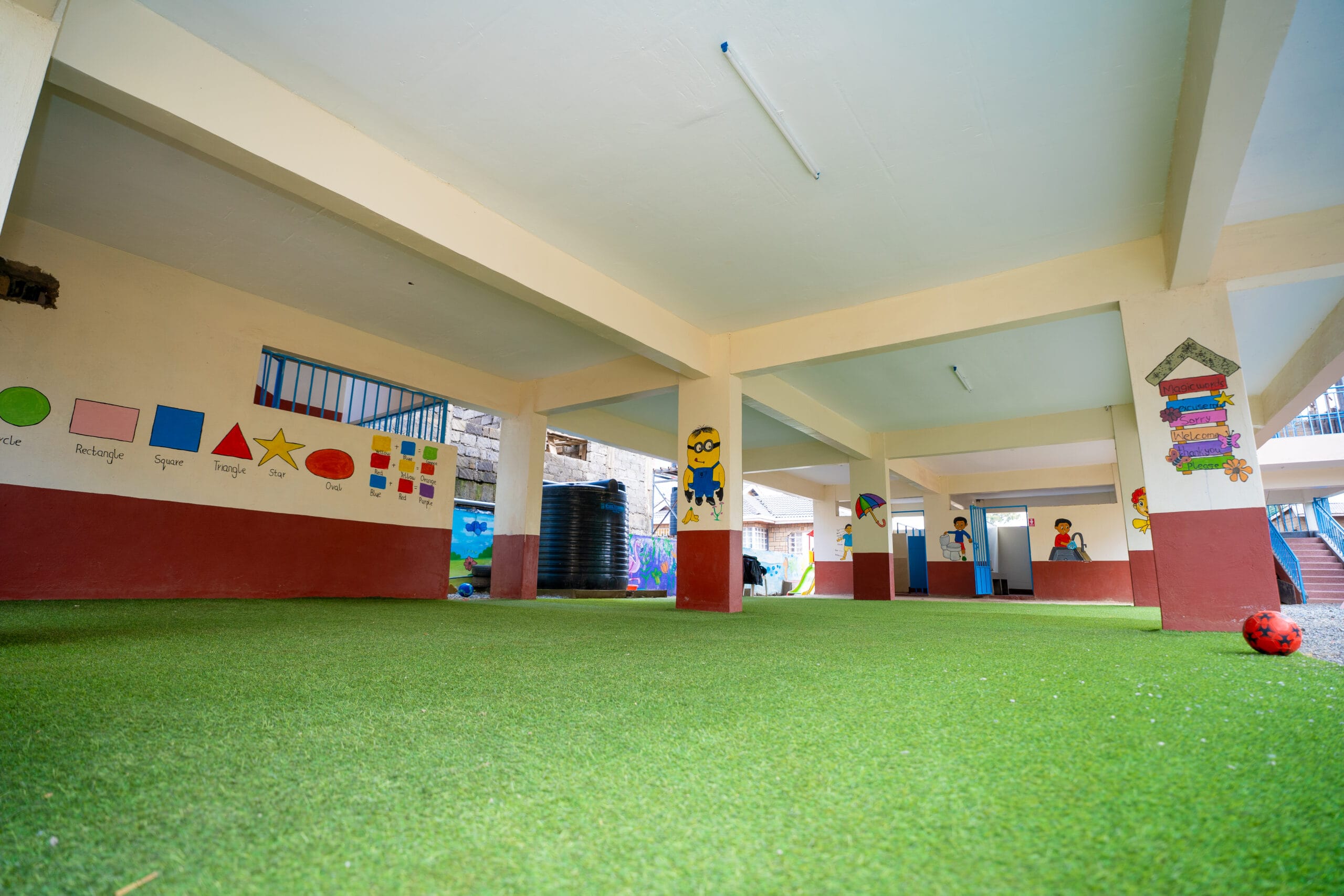 Covered school play area with artificial grass, educational wall paintings, and a football.