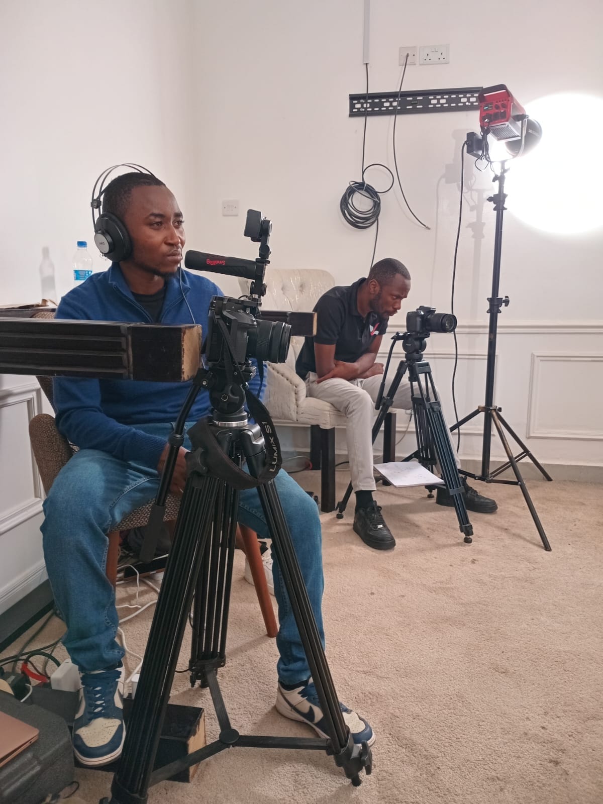 Two camera operators working with video cameras, tripods, headphones, and studio lighting during an indoor production.